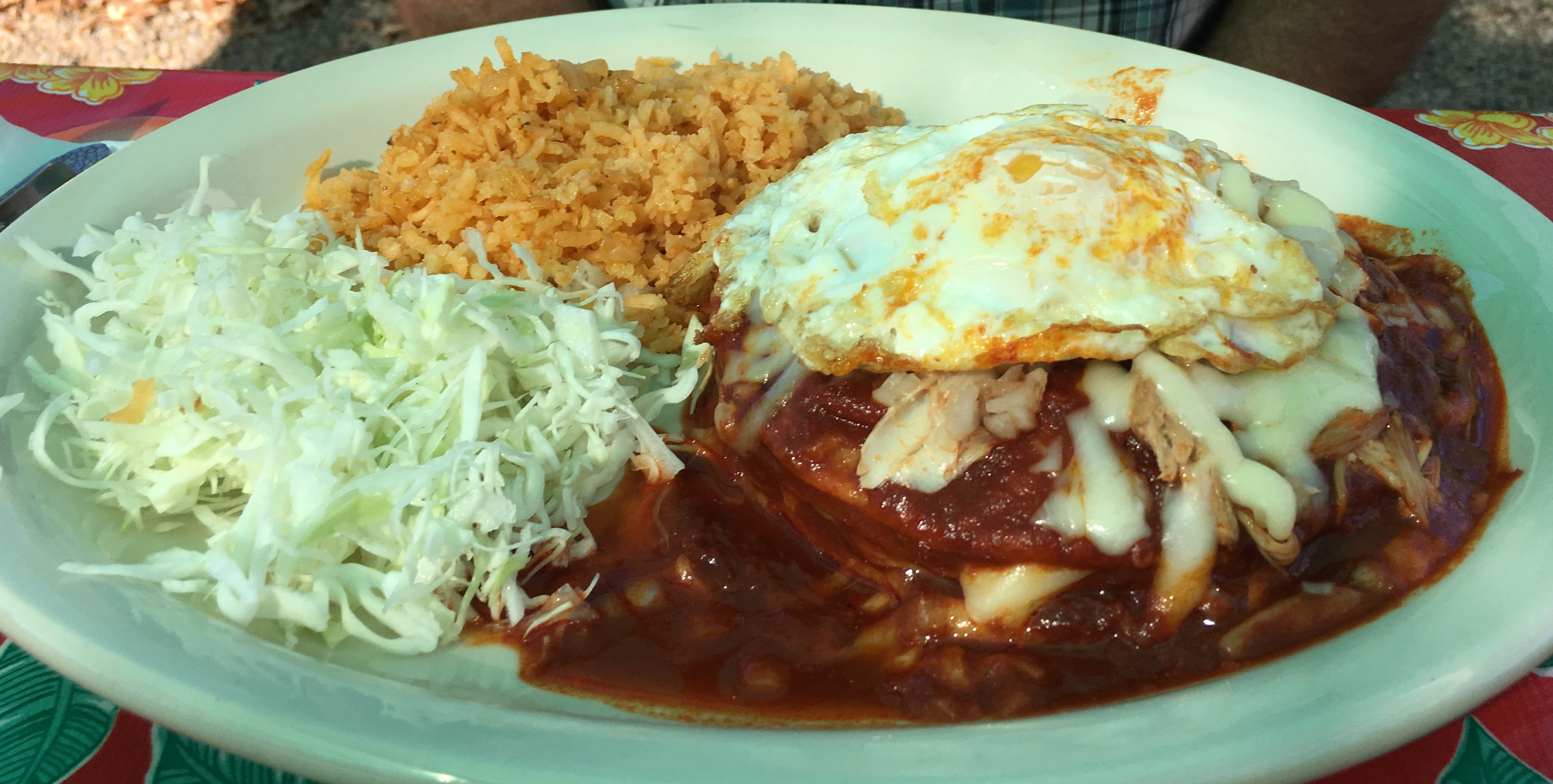 Chicken enchiladas with red sauce and an egg on top, with rice and cabbage.